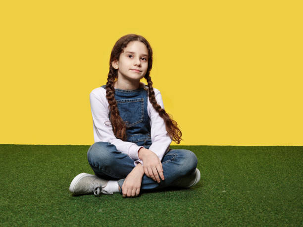 istock Cute little girl is lying down on artificial grass in the studio, yellow background. 1386823840