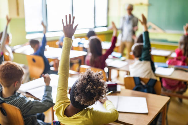 istock Rear view of elementary students raising hands on a class. 1386825269
