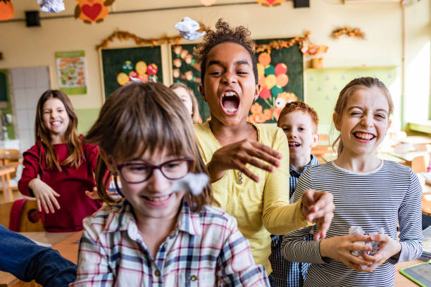 istock School kids feeling frustrated of using papers on a class and throwing them towards the camera. 1386825328