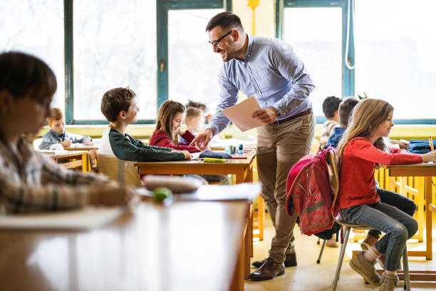 istock Happy teacher helping his student on a class at elementary school. 1386825431