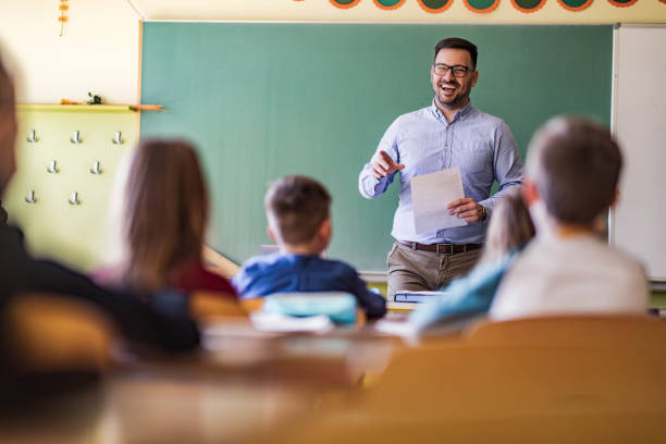 istock Happy male teacher giving a lecture at elementary school. 1386826068