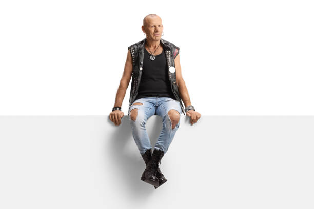 istock Punk man with ripped jeans sitting on a panel and looking at camera 1386827585