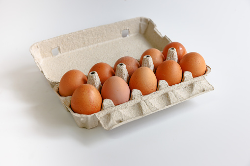 Ten eggs in open carton on white background, organic food, studio shot