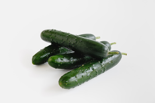 Small heap of four green cucumbers on white background, organic food, studio shot