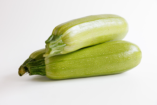 Close-up on small heap of three light green zucchini with stem on white background, organic food, studio shot