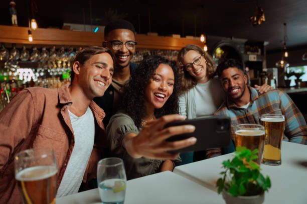 Group of young adult friends eating dinner at restaurant taking selfies Group of young adult friends eating dinner at restaurant taking selfie with cellular device. High quality photo happy hour stock pictures, royalty-free photos & images