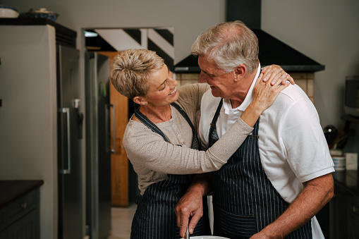 romantic elderly couple hugging in kitchen cooking . High quality photo
