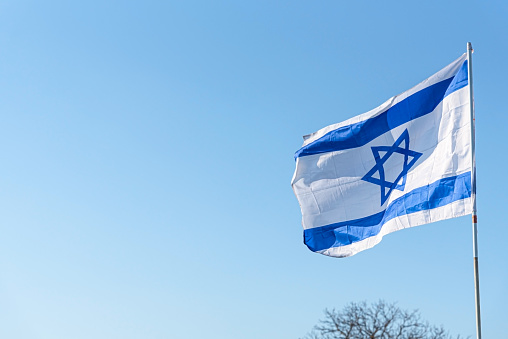 Flag of Israel on blue sky background. The Israeli Flag waving in the wind. Symbol of the Jewish state
