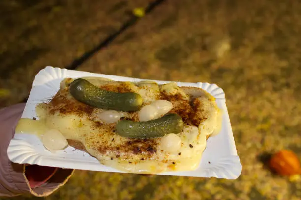 Raclette cheese on bread with onion and cucumber (gherkins) pickles bought at  Fasnacht carnival food stall in basel stadt Switzerland. Background has Fasnacht carnival papers on the road. Street food