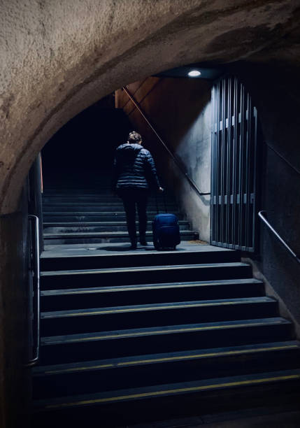 Woman travelling alone on Lisbon subway pictured walking up dark stairway with luggage.