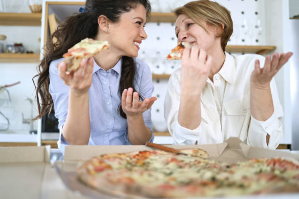 Mother and daughter having pizza at home in the kitchen counter stock photo