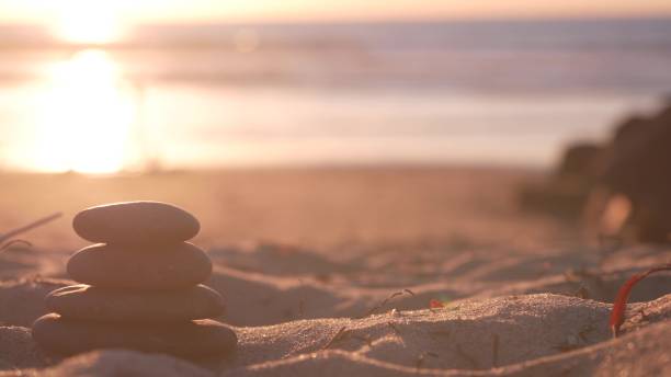istock Stack of pebble stones, sandy ocean beach, sunset sky. Rock balancing by water. 1386837903