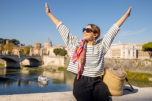Woman enjoying beautiful view of Rome city and Vatican standing on the bridge on a sunny autumn day. Elegant woman wearing stripped blouse and shawl in hair. Concept of italian lifestyle and travel