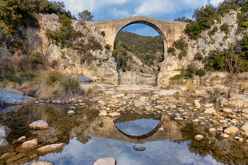 View of an ancient bridge Pont de Llierca in Catalonia, Spain. This beautiful bridge, paved with sandstone slabs, is in use since the 14th century.