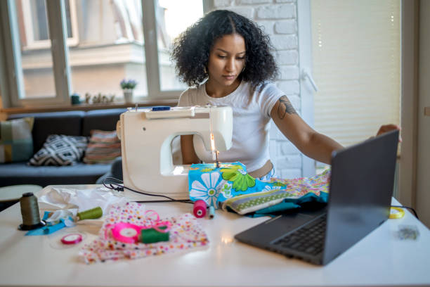 joven costurera empresaria usando computadora portátil y máquina de coser - thread needle sewing red fotografías e imágenes de stock