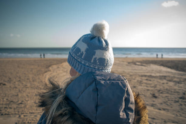 A young woman looks across a beach and out to sea in winter sun.