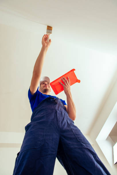 istock Worker in blue uniform is painting wall in the white 1386850673