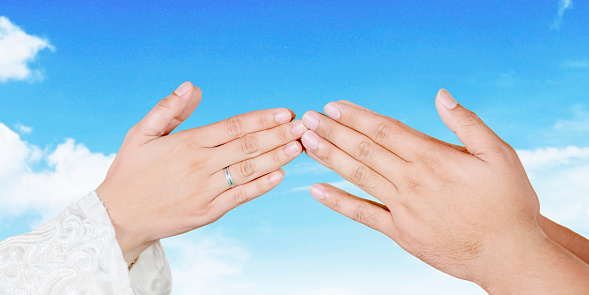 Hands of Muslim young couple handshaking and forgiving to each other during Eid Mubarak with blue sky background. Shot at outdoors