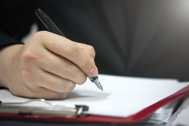 istock businessman hand holding a pen to write on documents. 1386851421