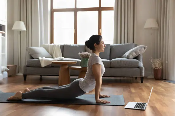 Photo of Happy young indian woman stretching muscles, enjoying online yoga class.
