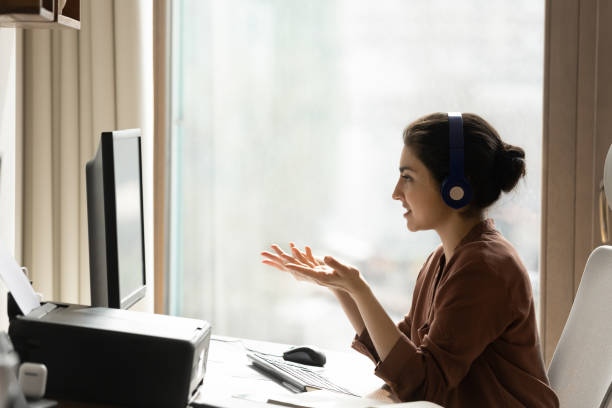 Happy beautiful young indian businesswoman holding video call meeting. Happy beautiful busy indian ethnicity businesswoman in headphones looking at computer monitor, holding distant web camera meeting with colleagues using video call software application in home office. divergent movie review stock pictures, royalty-free photos & images