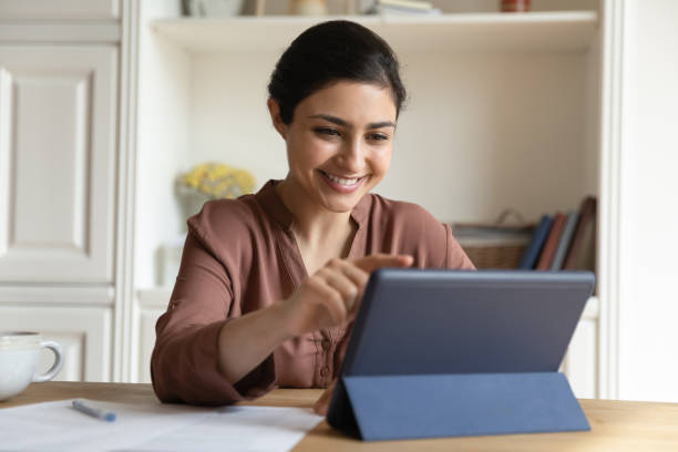 Happy indian woman using digital computer tablet. Happy attractive millennial indian ethnicity woman sitting at table, using digital computer tablet, enjoying web surfing information, choosing goods shopping in internet store, communicating online. divergent movie review stock pictures, royalty-free photos & images