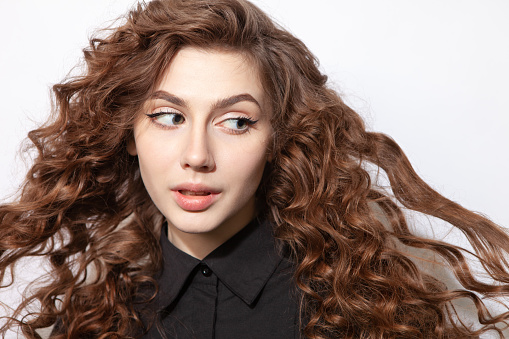 Close-up studio portrait of a 20 year old woman with curly brown hair in a black shirt on a white background