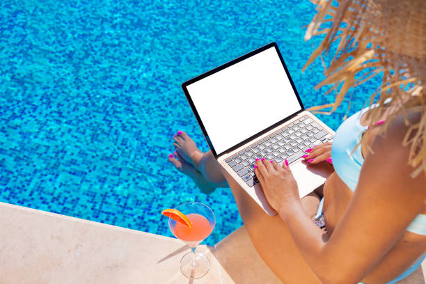 istock Woman using laptop by the pool, blank white screen mockup 1386857061