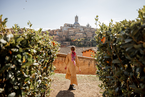 Stylish woman walks on background of cityscape of Siena old town. Concept of travel famous cities in Tosacny region of Italy