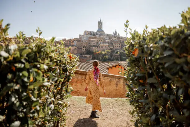 Photo of woman walks on background of cityscape of Siena old town in Italy