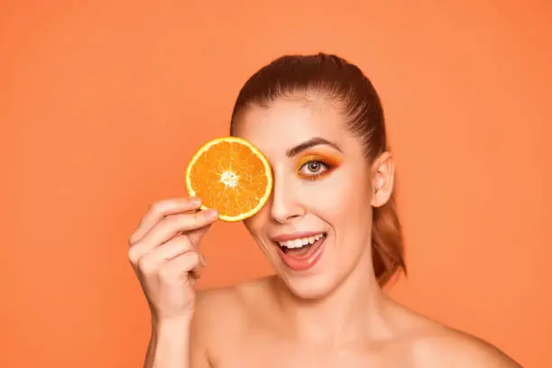Closeup portrait of beautiful smiling girl , holding half of oranges near face, isolated on orange background. Beauty and health care concept. High quality photo.