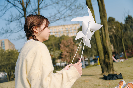 A beautiful asian girl sitting on a blanket on a sunny day playing with a paper windmill