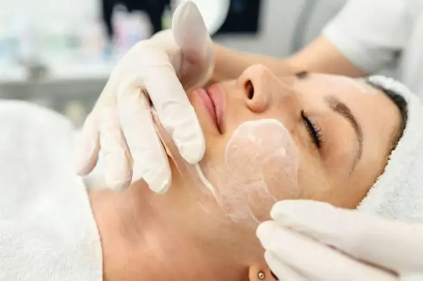 Cosmetician holding a jar of face lotion in a hand