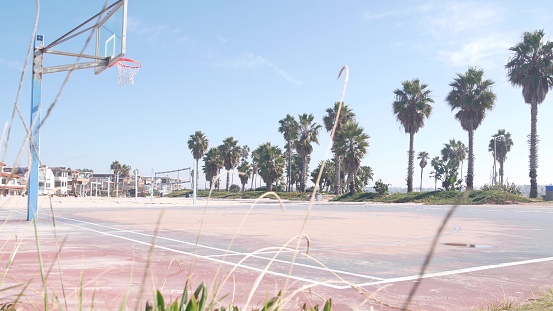 Basketball court with hoop, net and backboard for basket ball game on beach, California coast, USA. Sport field for streetball or netball players, palm trees on ocean shore. Mission beach, San Diego.