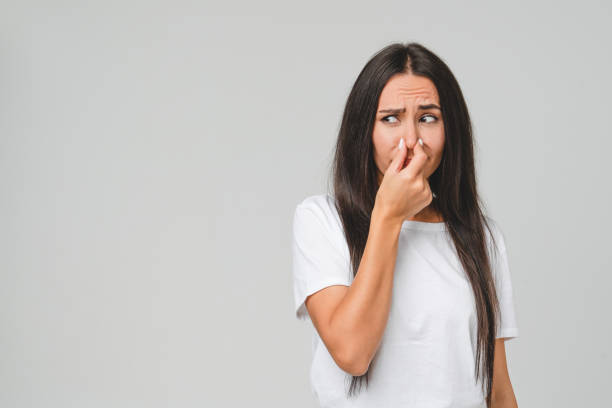 jeune femme caucasienne triste déçue en t-shirt blanc sentant puant, fermant le nez avec une main à cause d’une odeur nauséabonde isolée dans un fond gris - sentir photos et images de collection