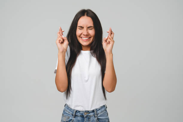 白いtシャツを着た白人の若い女性が幸運、成功、賭けの宝くじでお金を獲得するために指を交差させることを願って 灰色の背景で隔離されたオンラインカジノ - lying in wait ストックフォトと画像