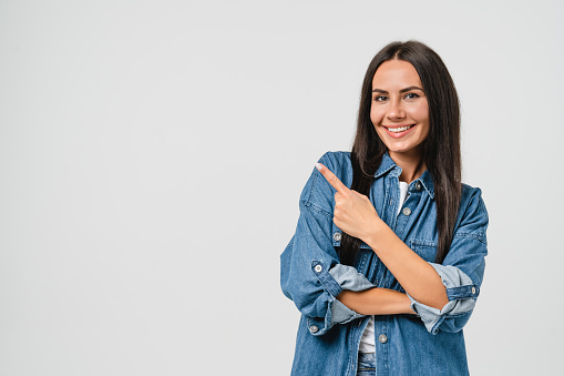 Happy smiling caucasian young woman with toothy white smile looking at camera pointing showing copy space free space isolated in white background