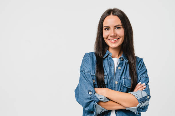 sonriente feliz joven caucásica con camisa vaquera mirando a cámara con los brazos cruzados aislados en fondo blanco. sonrisa dentada, concepto de estomatología odontológica - clipping path fotos fotografías e imágenes de stock