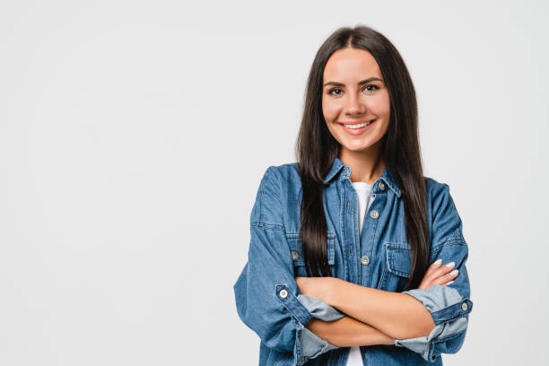 smiling happy caucasian young woman in denim shirt looking at camera with arms crossed isolated in white background. toothy smile, dentistry stomatology concept - woman stockfoto's en -beelden