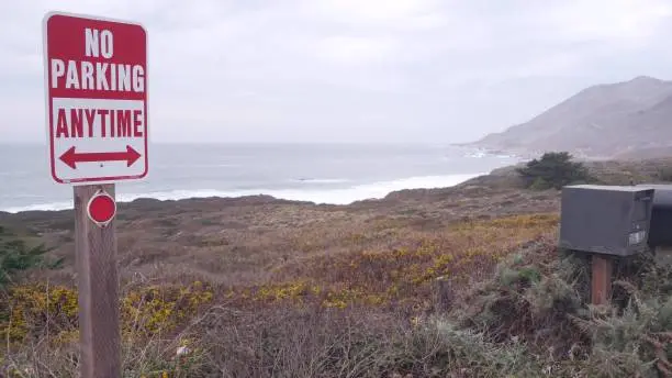 Photo of No parking road sign, pacific coast highway. Ocean waves, foggy California beach