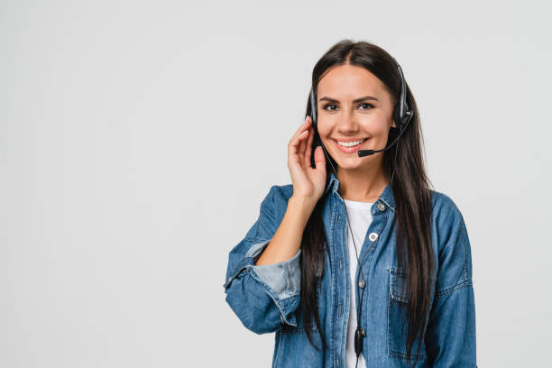 jeune femme caucasienne sympathique support informatique agent de support client hotline employé de la ligne d’assistance téléphonique dans un casque regardant la caméra tout en aidant le client client isolé en fond blanc - réceptionniste téléphonique photos et images de collection