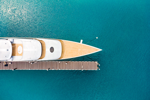 Aerial view of a luxurious white modern expensive yacht moored to a long pier in a bay with crystal clear turquoise ocean water. Close-up. Tourism concept