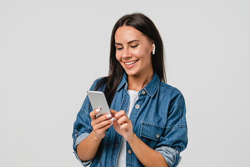 Smiling caucasian young woman listening to the podcast e-book music song singer rock band in earphones, choosing sound track on cellphone isolated in white background