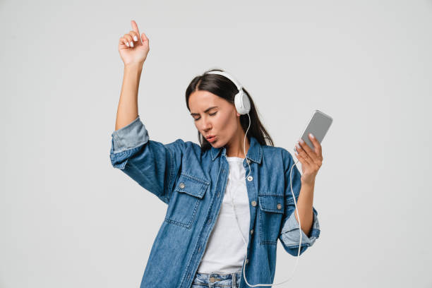 Energetic caucasian young woman girl dancing singing listening to the music podcast song singer sound track e-book in headphones earphones on cellphone isolated in white background stock photo