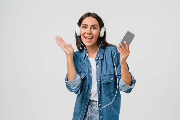 Photo of Excited active caucasian young woman girl listening to music in headphones earphones, dancing singing choosing sound track podcast e-book isolated in white background