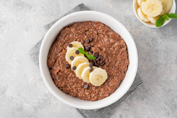 schokoladen-haferflockenbrei mit banane und schokoladenstückchen oben drauf in einer weißen schüssel. gesundes frühstück. speicherplatz kopieren. - haferbrei stock-fotos und bilder