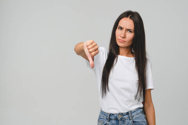 Negative opinion concept. Caucasian young woman in white T-shirt showing thumb down for unsatisfactory , bad quality concept isolated in grey background. Negative opinion concept. Caucasian young woman in white T-shirt showing thumb down for unsatisfactory , bad quality concept isolated in grey background. thumbs down stock pictures, royalty-free photos & images