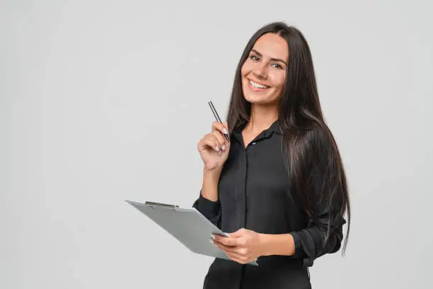 Photo of Smiling confident caucasian young businesswoman auditor writing on clipboard, signing contract document isolated in white background