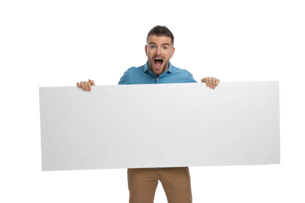 istock shocked casual guy with long white billboard in hands being surprised 1386866485