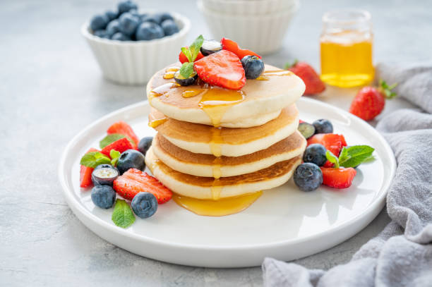istock A stack of delicious fluffy pancakes with berries and honey on a white plate on a gray concrete background. Copy space. 1386866768
